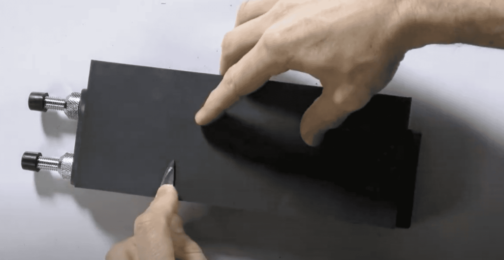 A close-up of hands holding a carving knife, skillfully working on a piece of wood secured in a clamp. This image captures the focus and precision needed in wood carving, perfect for highlighting wood carving classes and lessons.